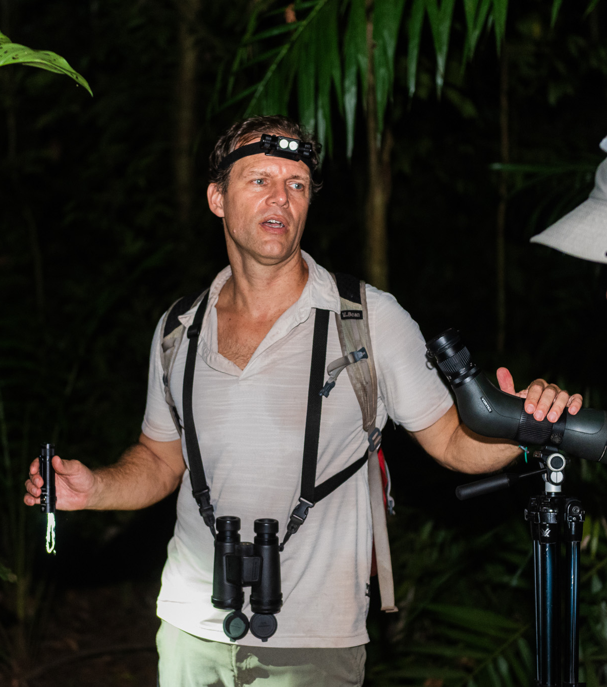 Ryan Meczkowski, the founder of Simbiotica Adventures, leading a night walk in the rainforest with his headlamp, binoculars, and spotting scope.